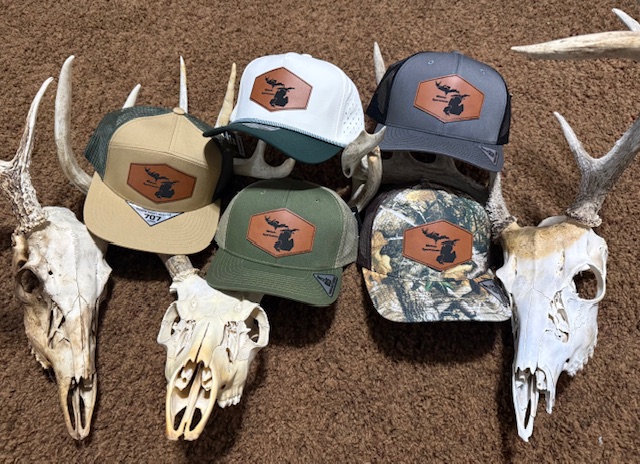 Six hats with logo, placed on animal skulls and antlers on brown surface.