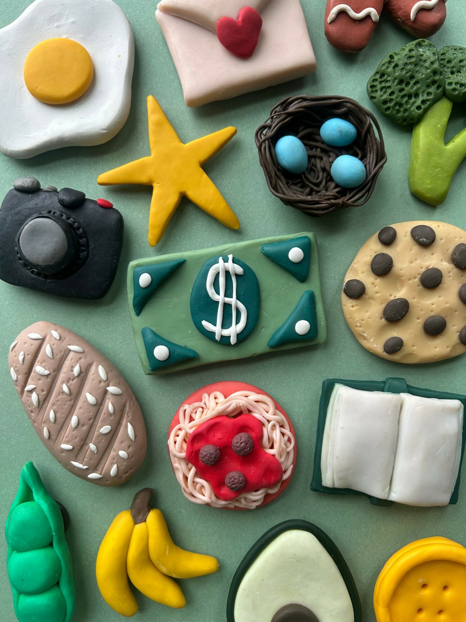 Colorful clay or fondant food and object shapes including a fried egg, star, camera, cookies, bananas, and avocado.