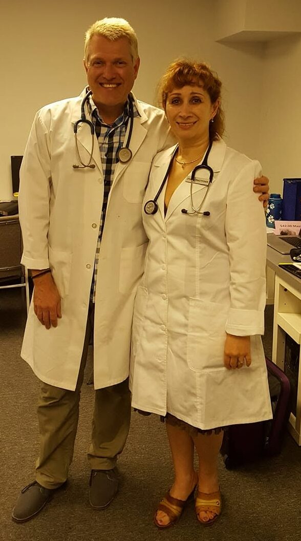 Two medical professionals, a man and a woman, in white coats with stethoscopes, standing together in a clinical setting.