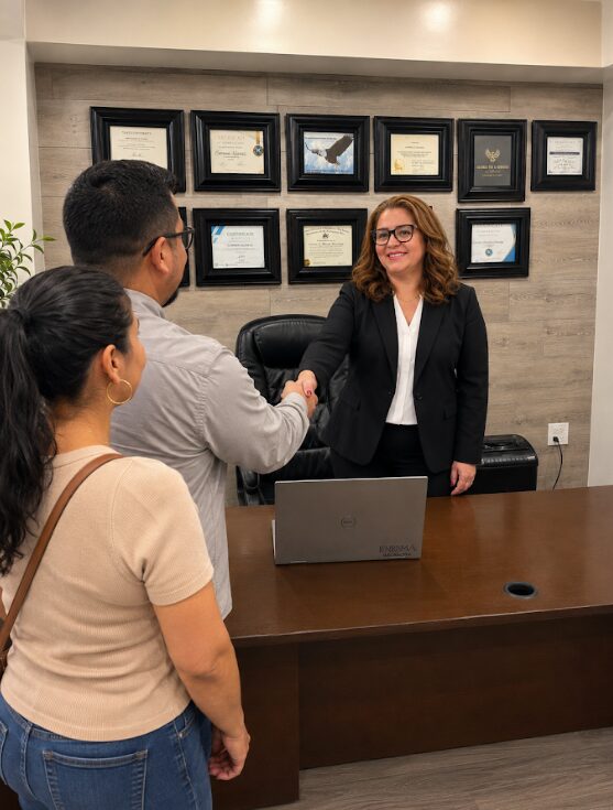 Three people in an office, woman in black blazer shaking hands with man, woman watching, certificates on wall behind.