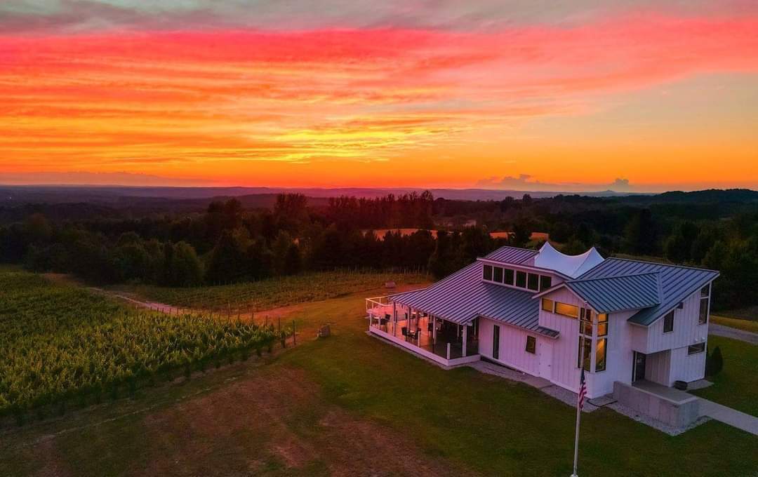 A white house with a blue roof is in a rural landscape during a colorful sunset sky.