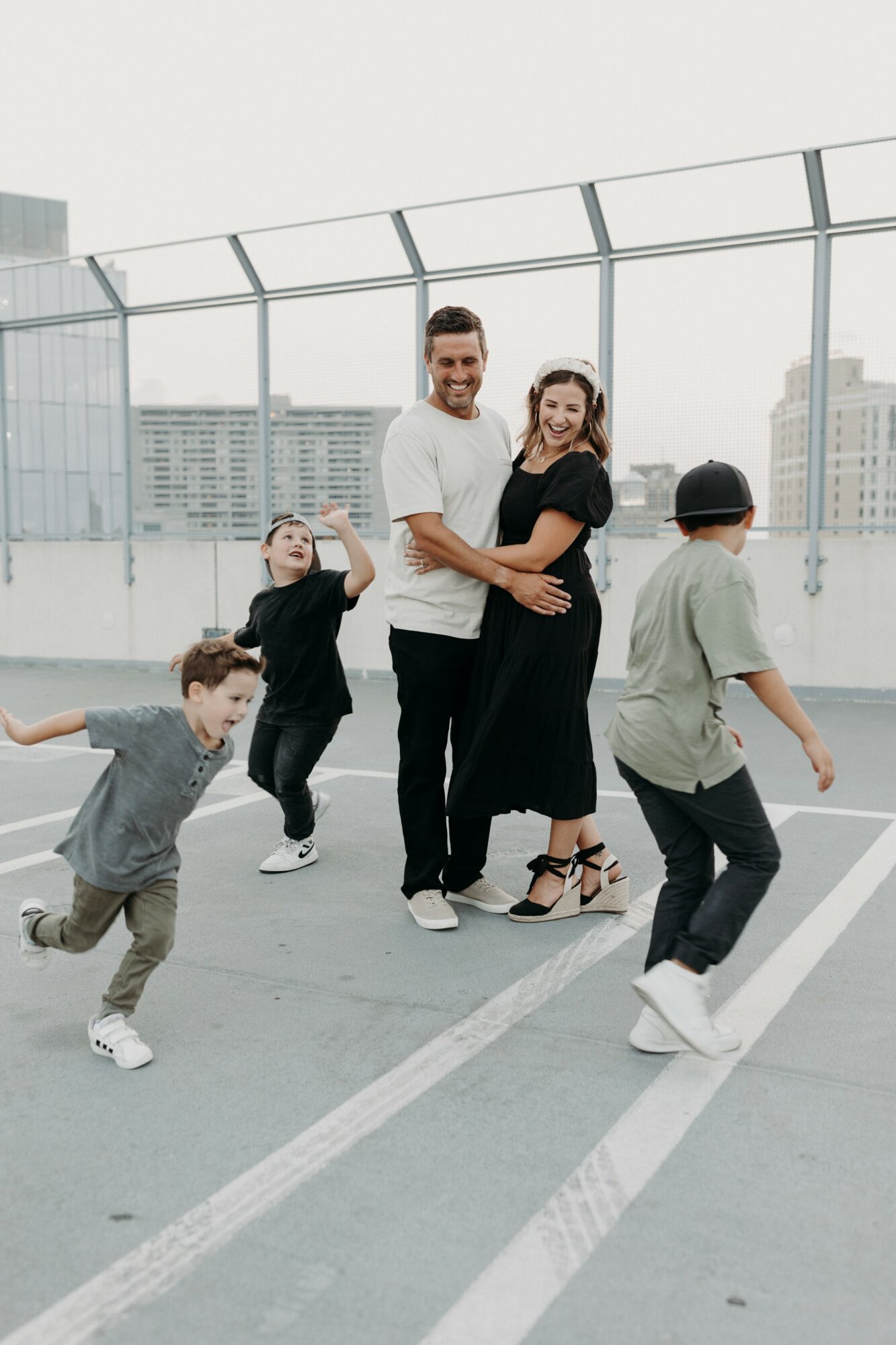 A group of people, including children and adults, playing and dancing on a rooftop parking lot with city buildings in background.
