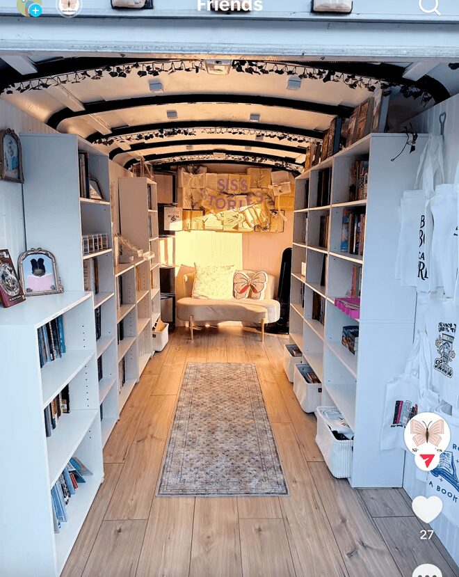 Bookshelves on both sides lead to a cozy seating area with a sofa and decorative pillows, under a curved ceiling with black accents.