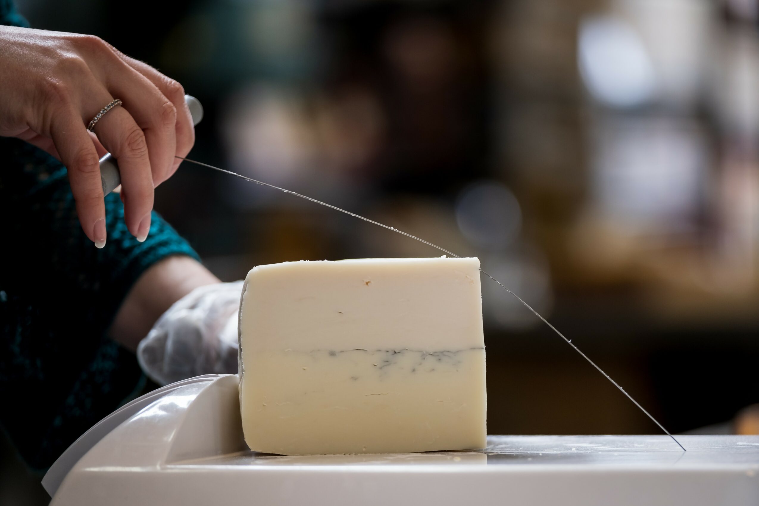Person holding a string and a block of cheese on a white plate, with a blurred background.