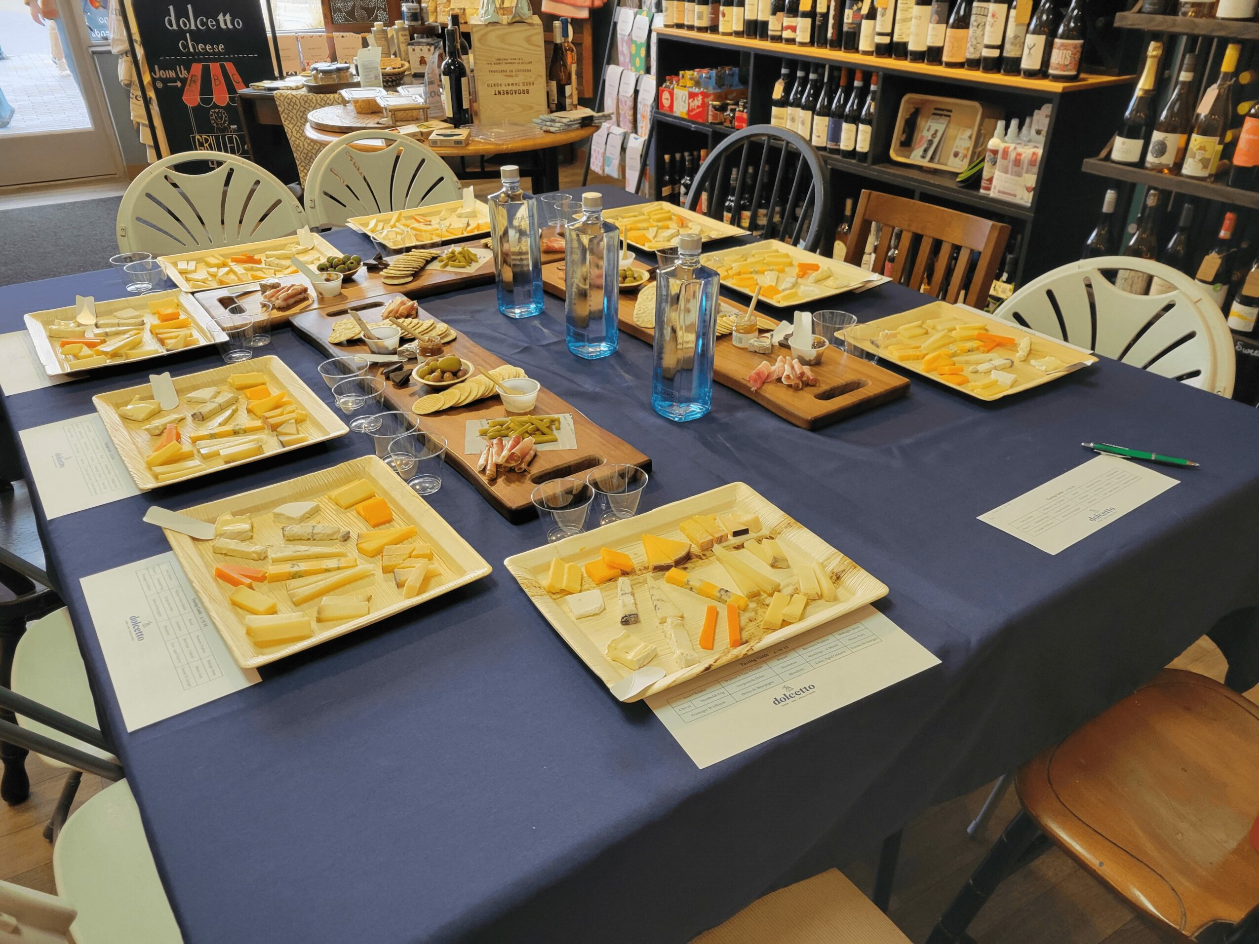 Table set with cheese, crackers, and water bottles in a bookstore or cafe, with chairs around it.