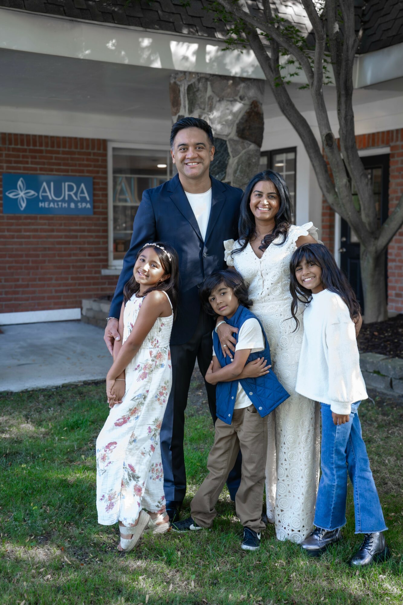 Group of five people, including a man and four women, standing outdoors in front of a building with trees, smiling.