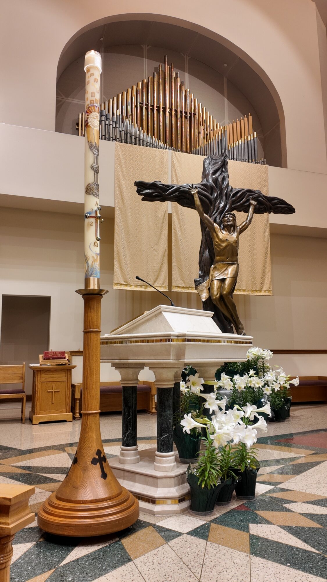 Religious altar with a crucifix, candles, flowers, and a wooden stand inside a church, with an organ in the background.