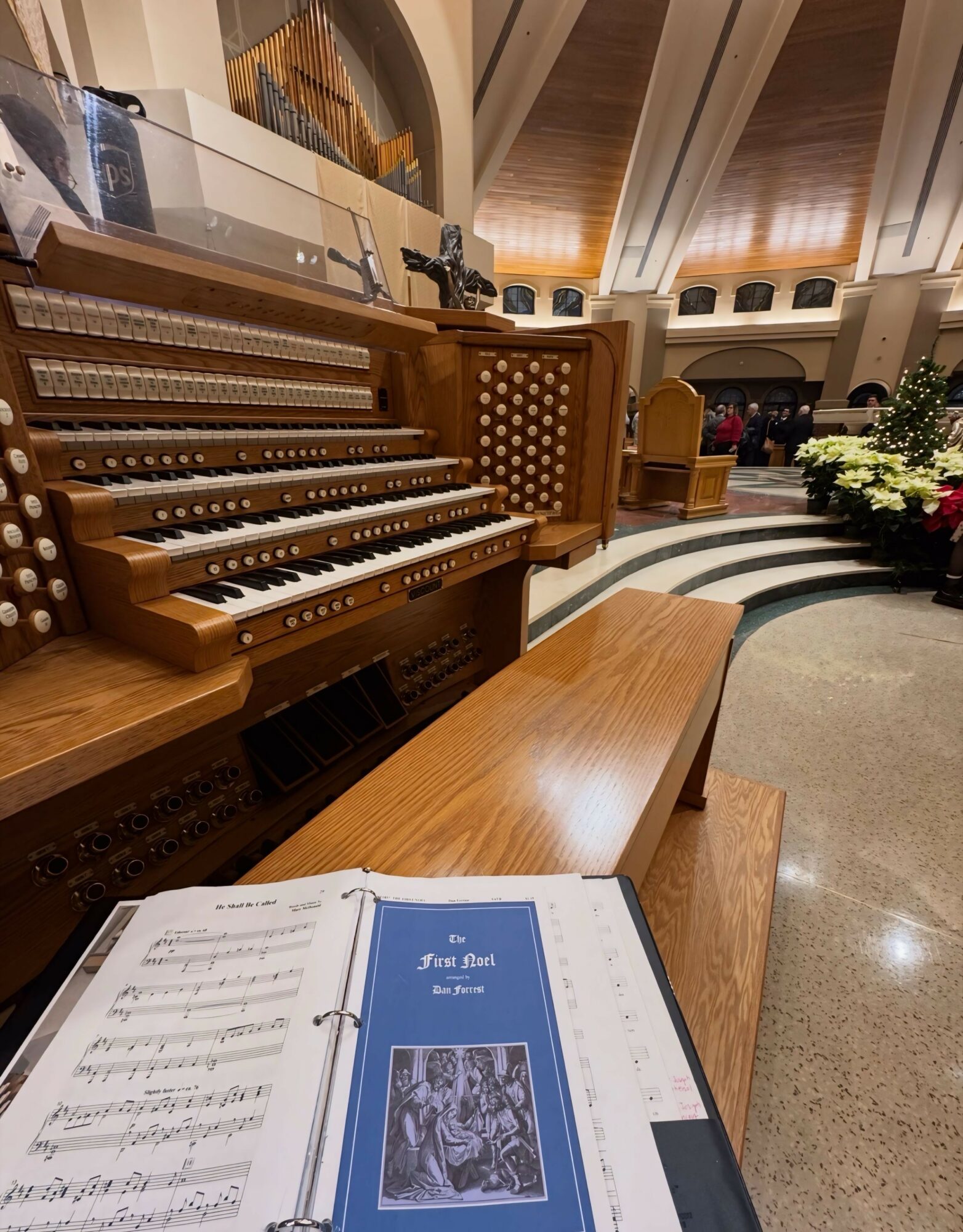 Organ with wooden bench in a spacious room, open music book on a stand, and decorative plants in the background.