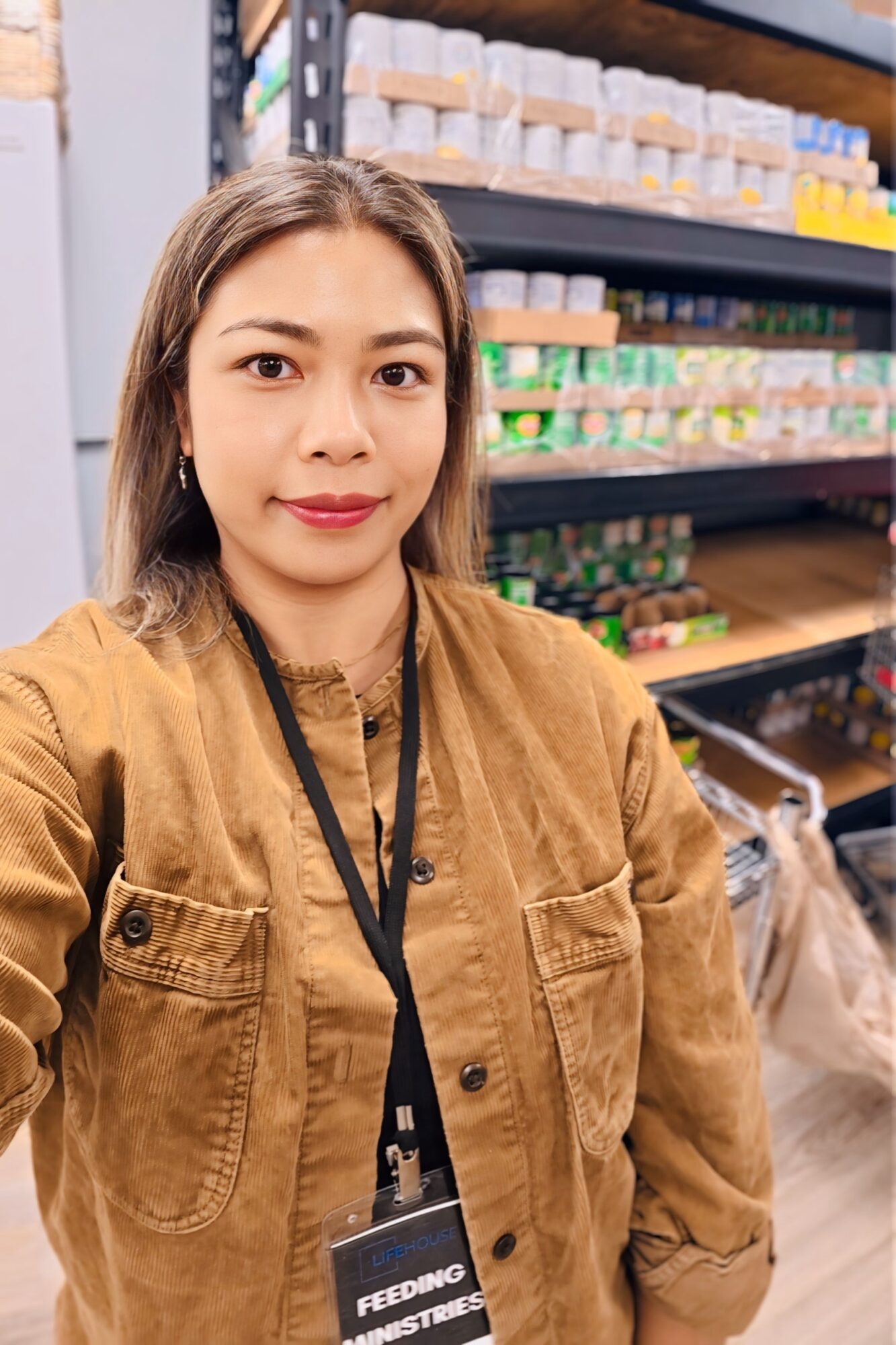 Woman taking a selfie in a store aisle with shelves of products behind her.