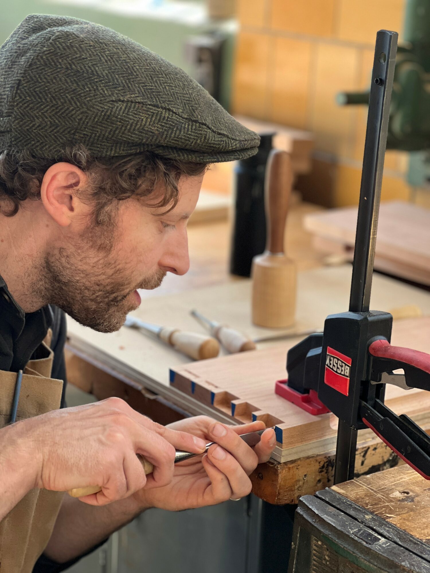 Man wearing a cap working on a woodworking project with clamps and tools on a workbench.