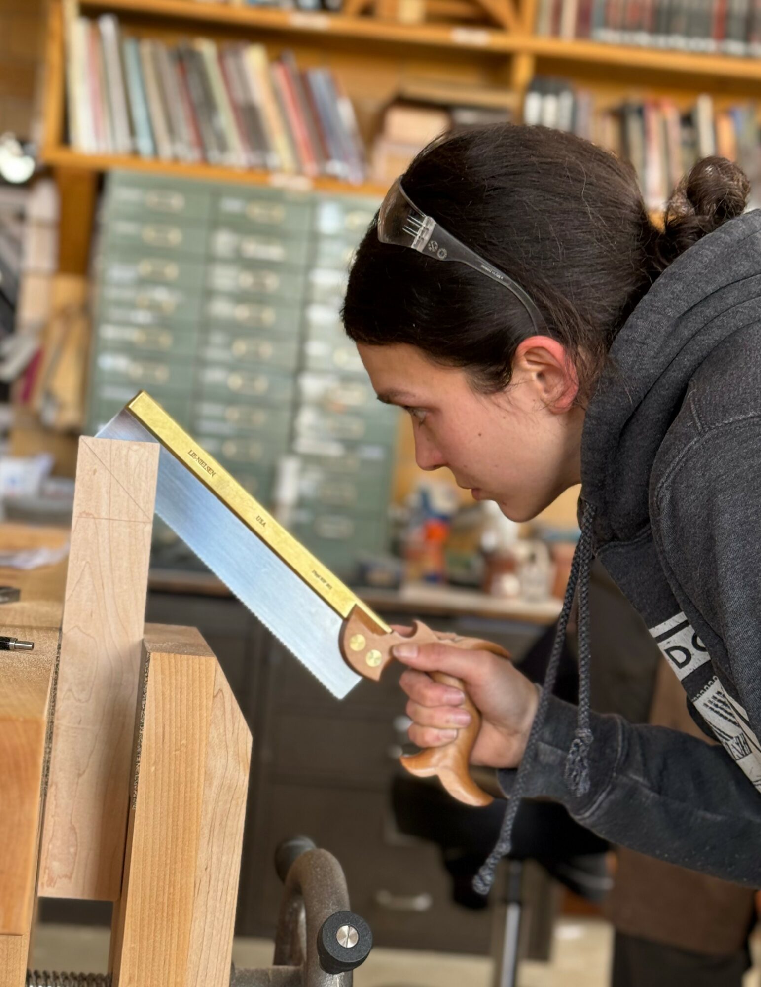 Person leaning over a wooden workbench, measuring with a yellow ruler in a workshop or library setting.