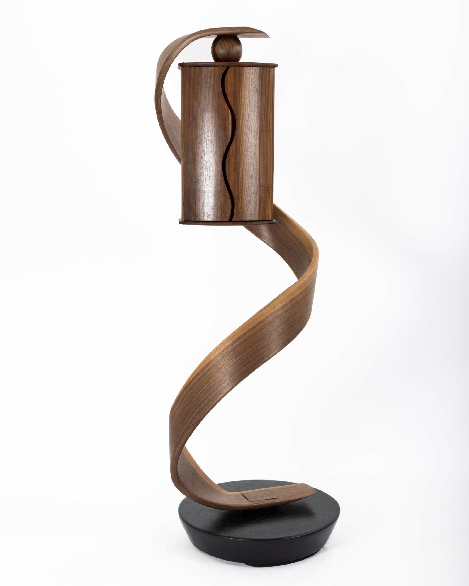 Wooden sculpture with a curved, spiral design on a black base, against a white background.