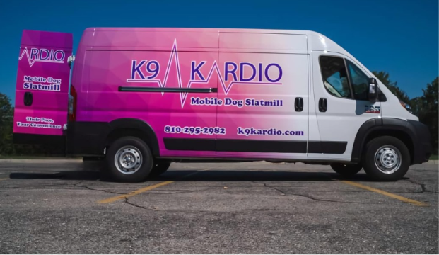 White and pink mobile dog grooming van with K9 KARDIO logo parked in a lot, blue sky background.