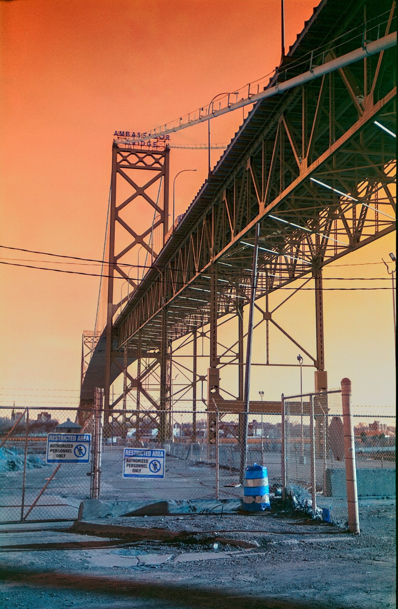 Bridge structure with support beams and construction fencing under a sunset sky.