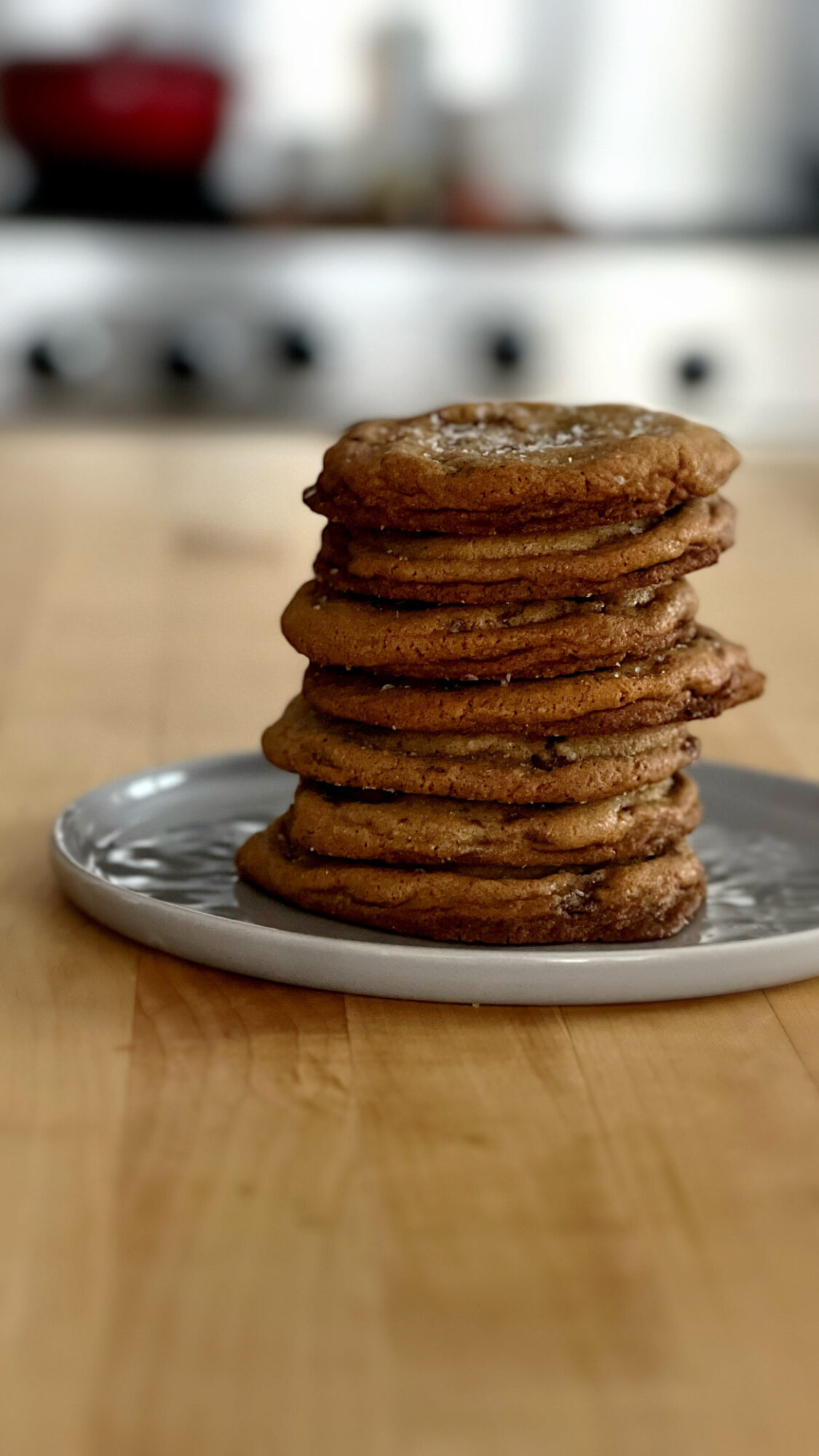 Stack of seven cookies on a white plate, on a wooden surface, with a blurred kitchen background.