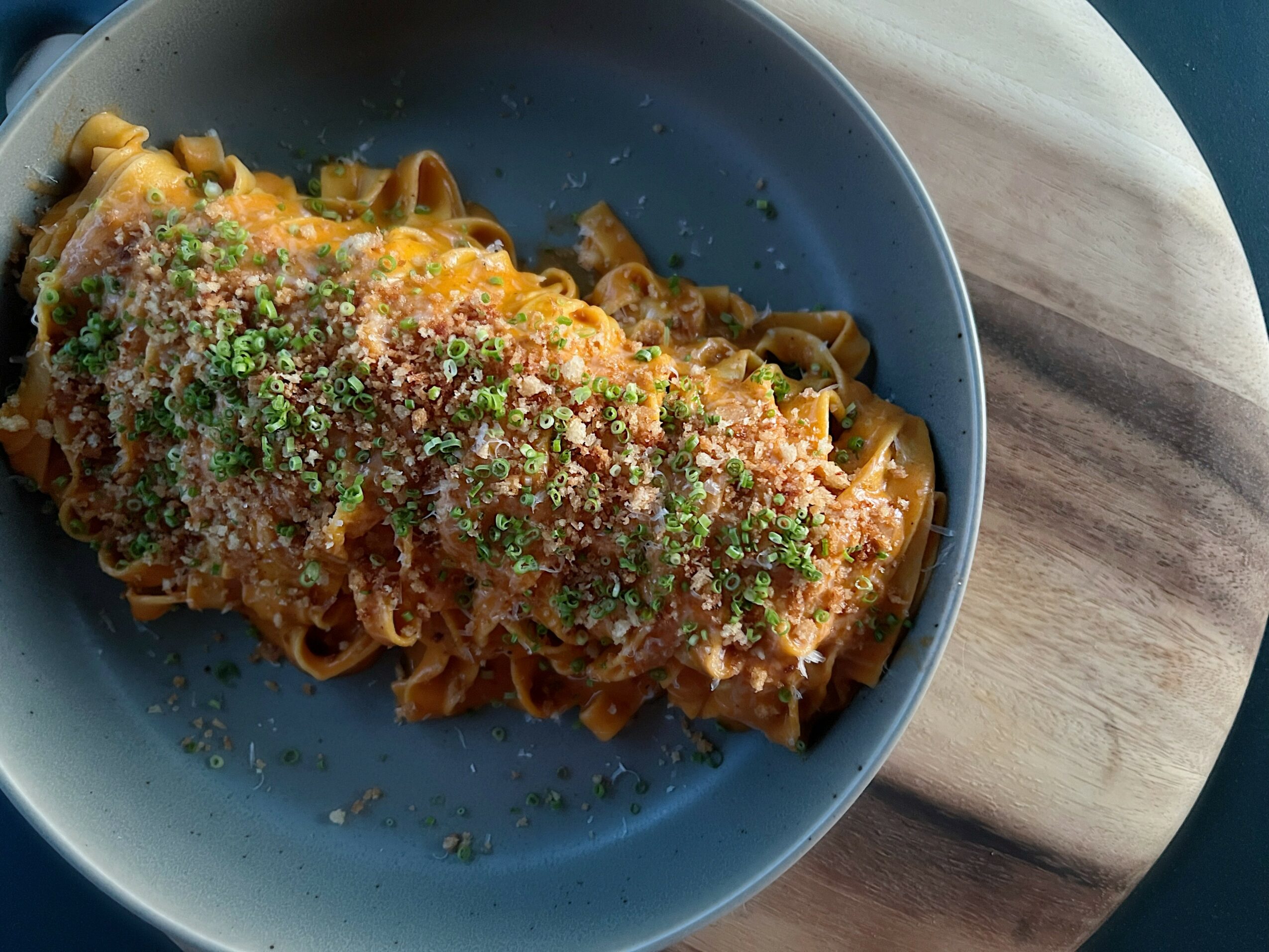 Plate of pasta with sauce and grated cheese, garnished with herbs, on a wooden surface.