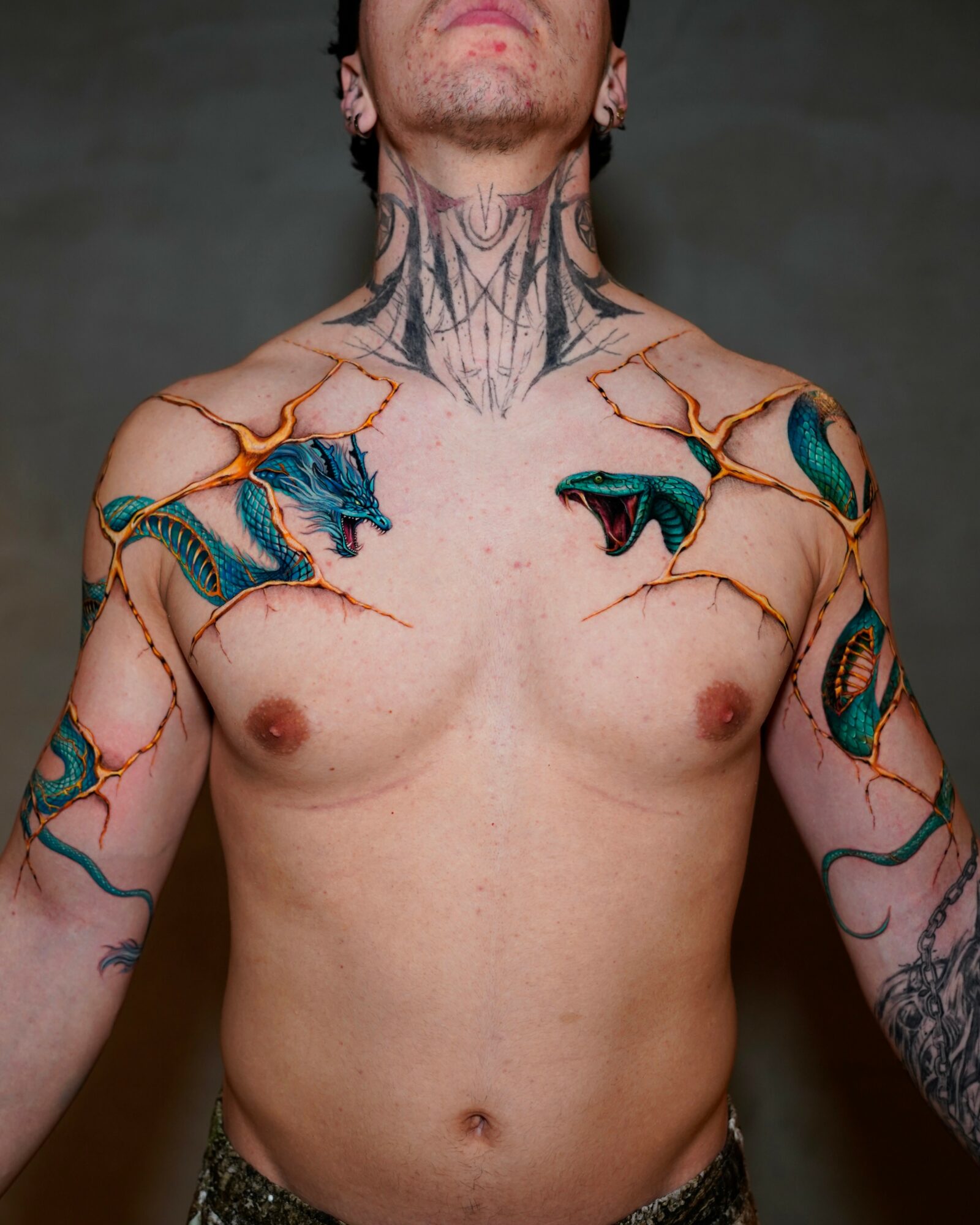 Person with tattoos on shoulders, chest, and neck, facing forward, with a dark background.