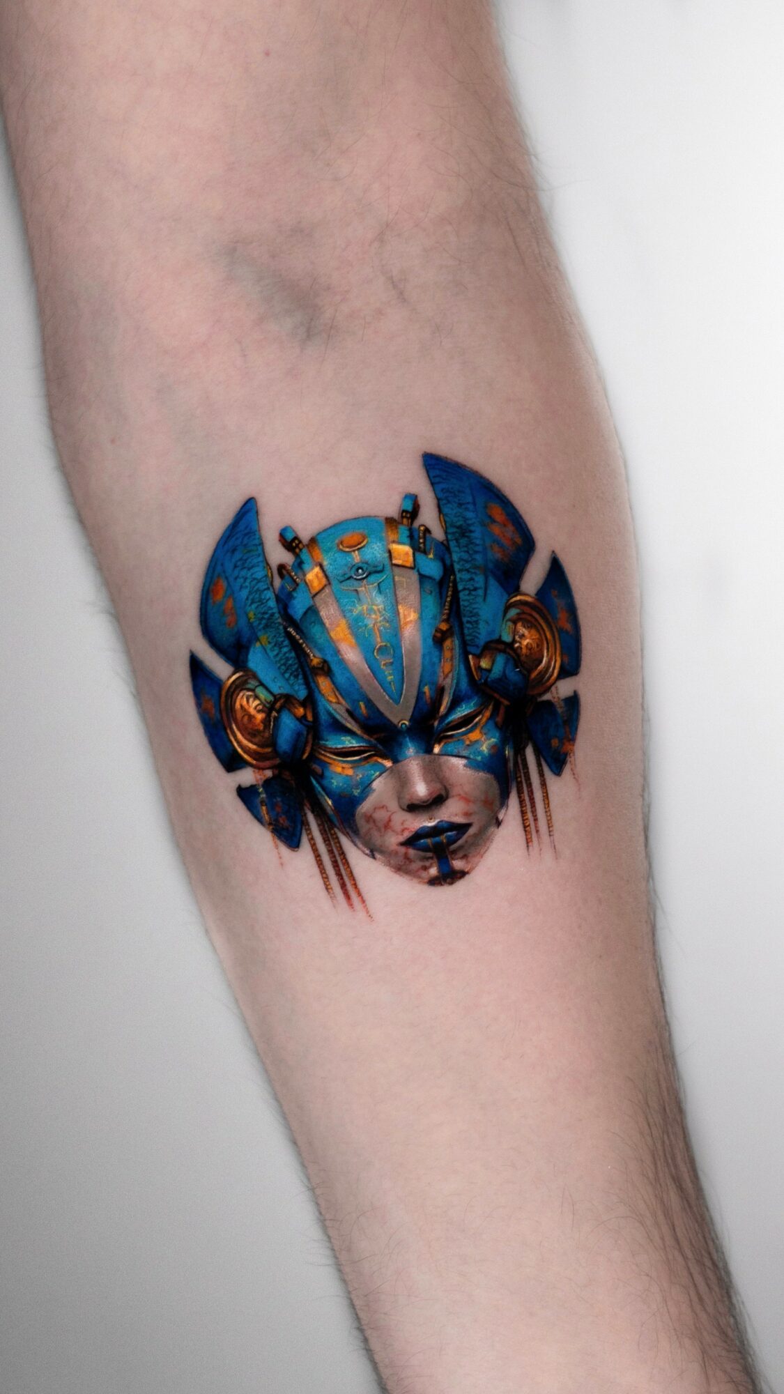 Tattoo of a blue and gold insect-like creature with a face on a person's arm.