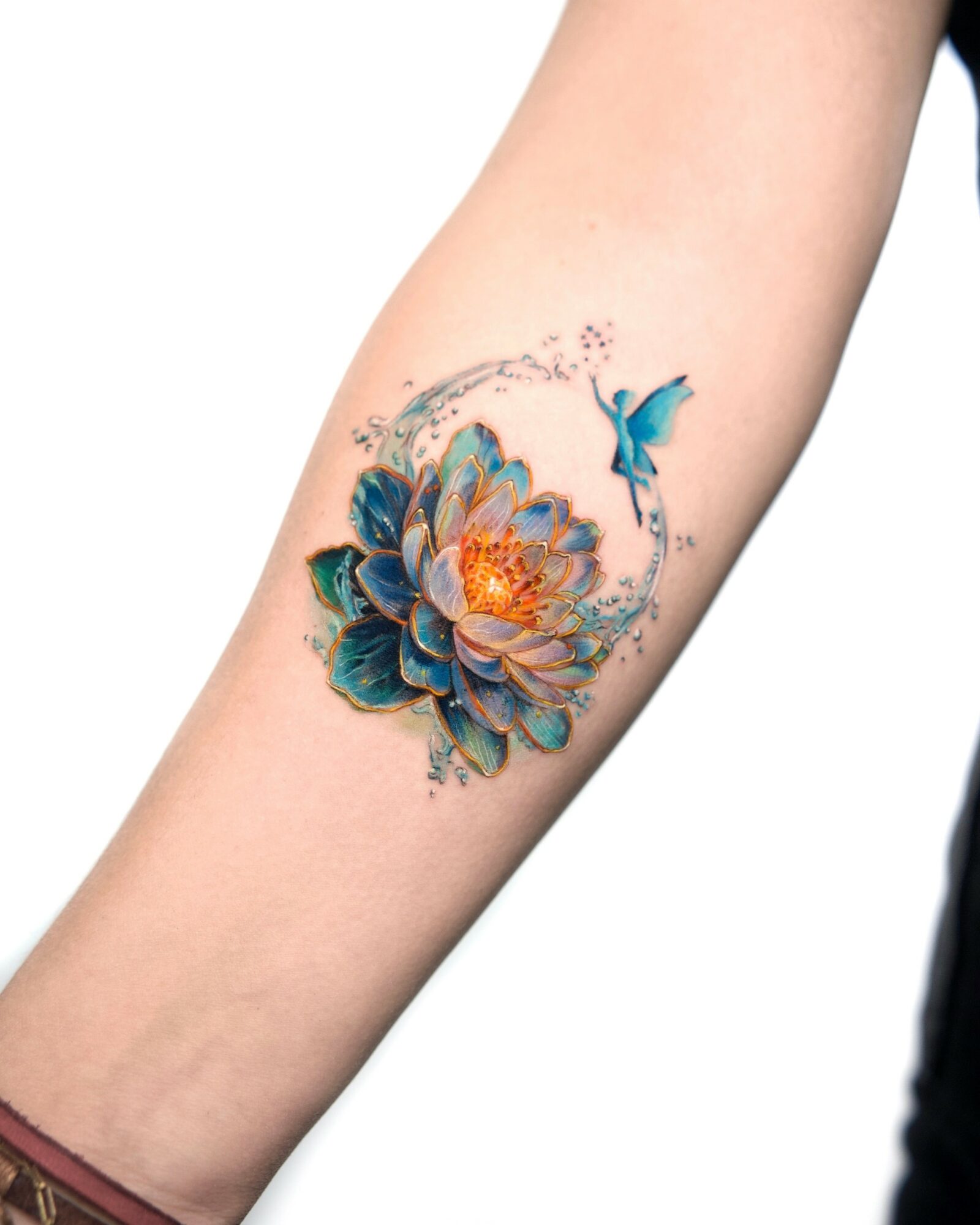 Tattoo of a large flower with a hummingbird on a person's arm, colorful and detailed, with splashes of paint around.