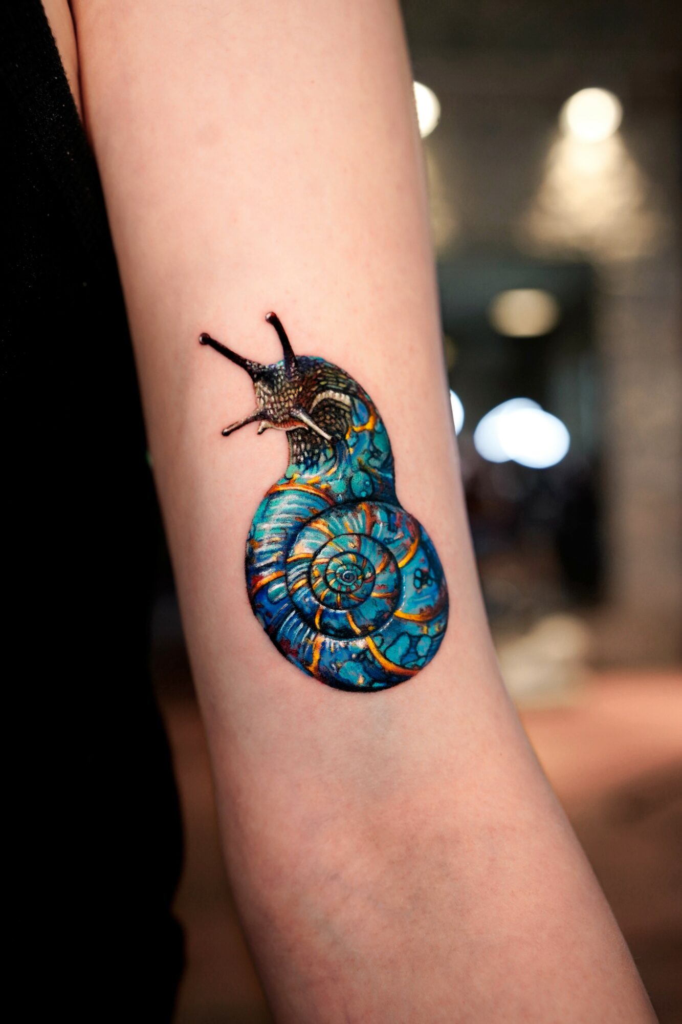 Colorful snail tattoo on person's arm with detailed shell and antennae, background blurred.