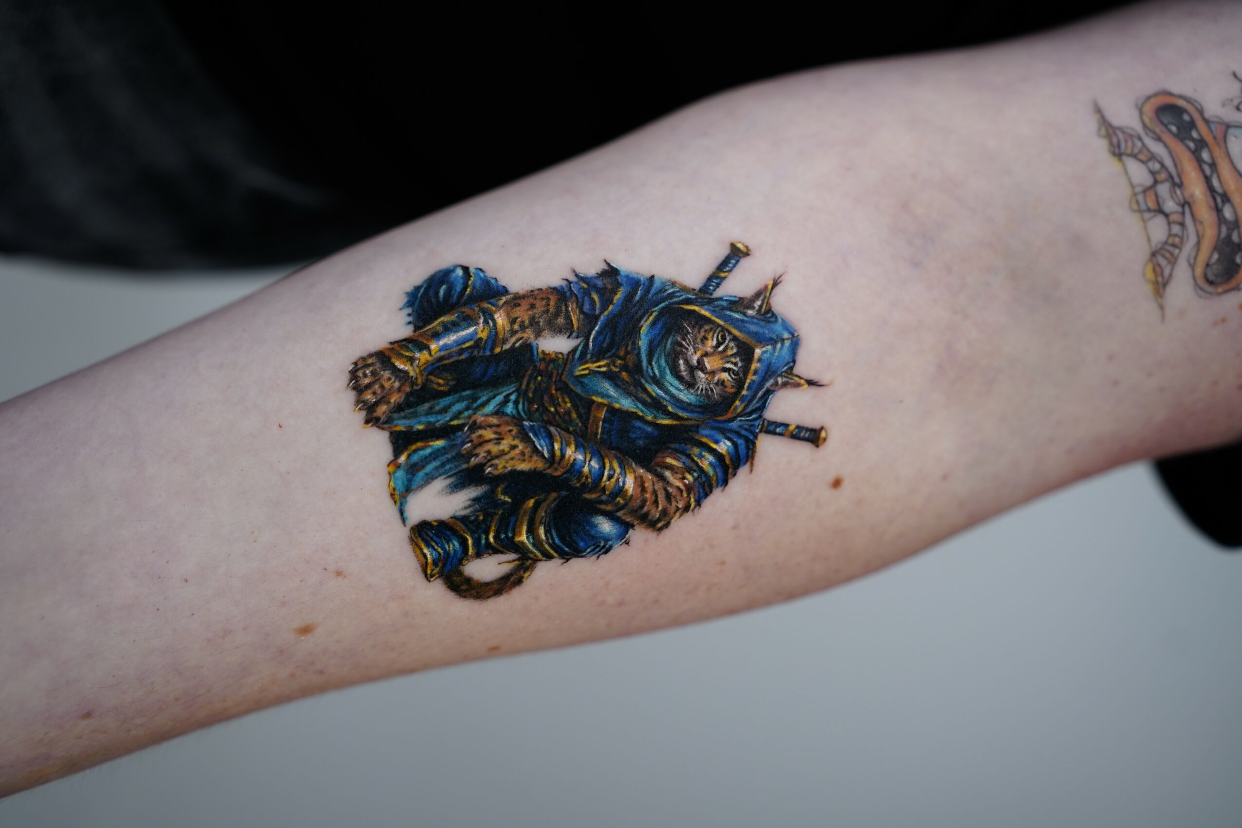Tattoo of a detailed blue and gold bee on a person's forearm, with another tattoo partially visible nearby.