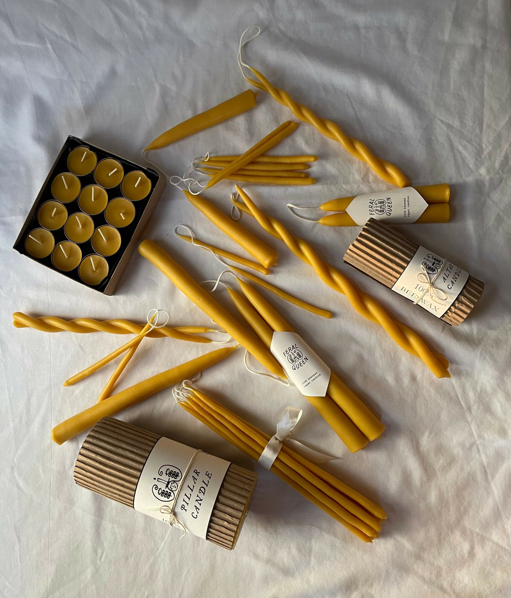 Various yellow candles, some in a black box, with packaging, arranged on a white surface.