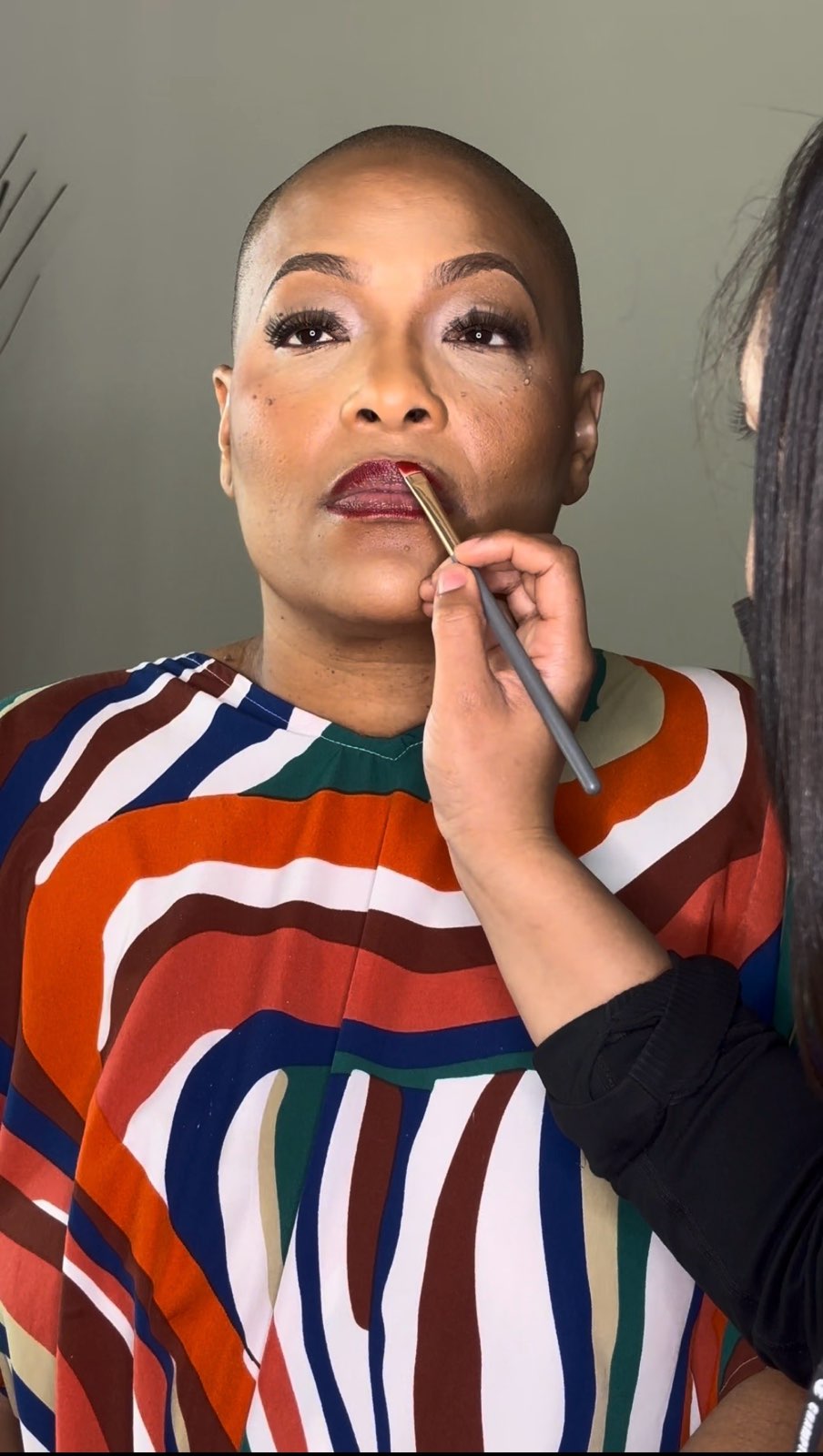 Woman with short hair having makeup applied, wearing a colorful striped top, looking slightly upward.