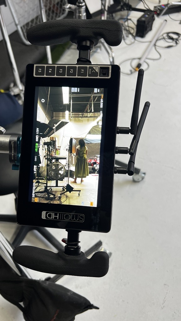 Device with screen showing a person in a yellow dress in a room with equipment and a person in the background.
