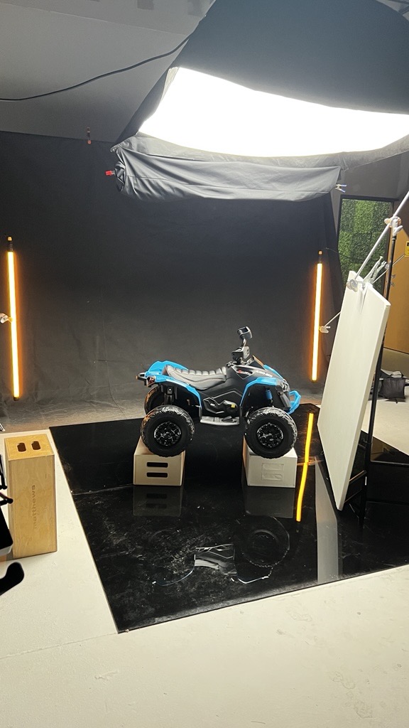 Small toy vehicle on display with black background and vertical light strips, surrounded by equipment and display stands.