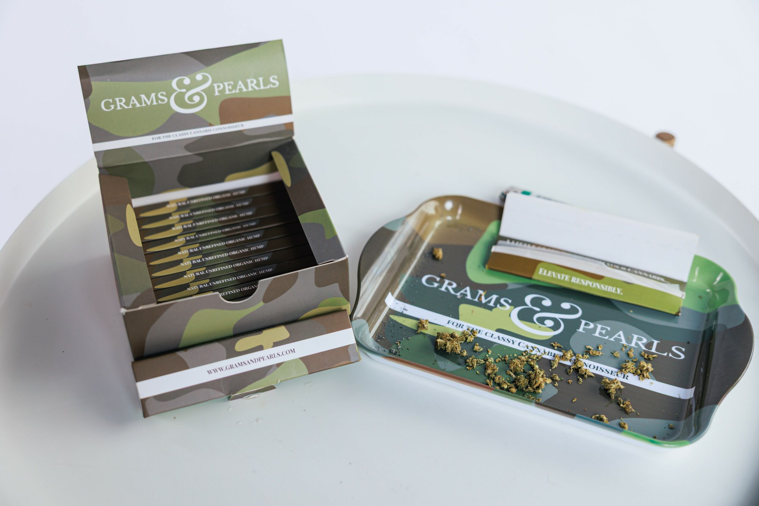 Box of earrings and a tray with jewelry and a small green object on a white surface.