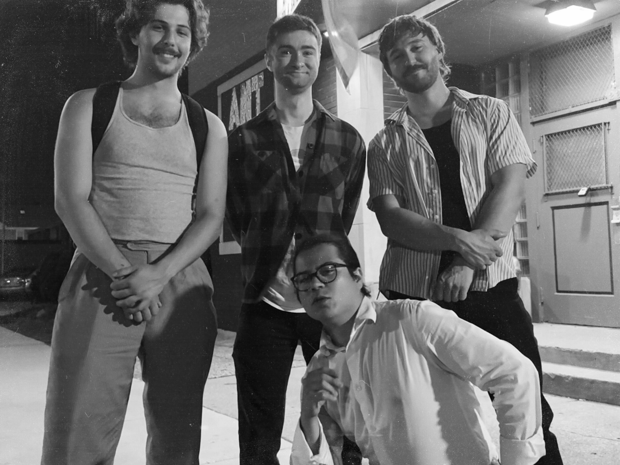 Four people standing together outdoors, one person crouching in front, all smiling, in black and white.