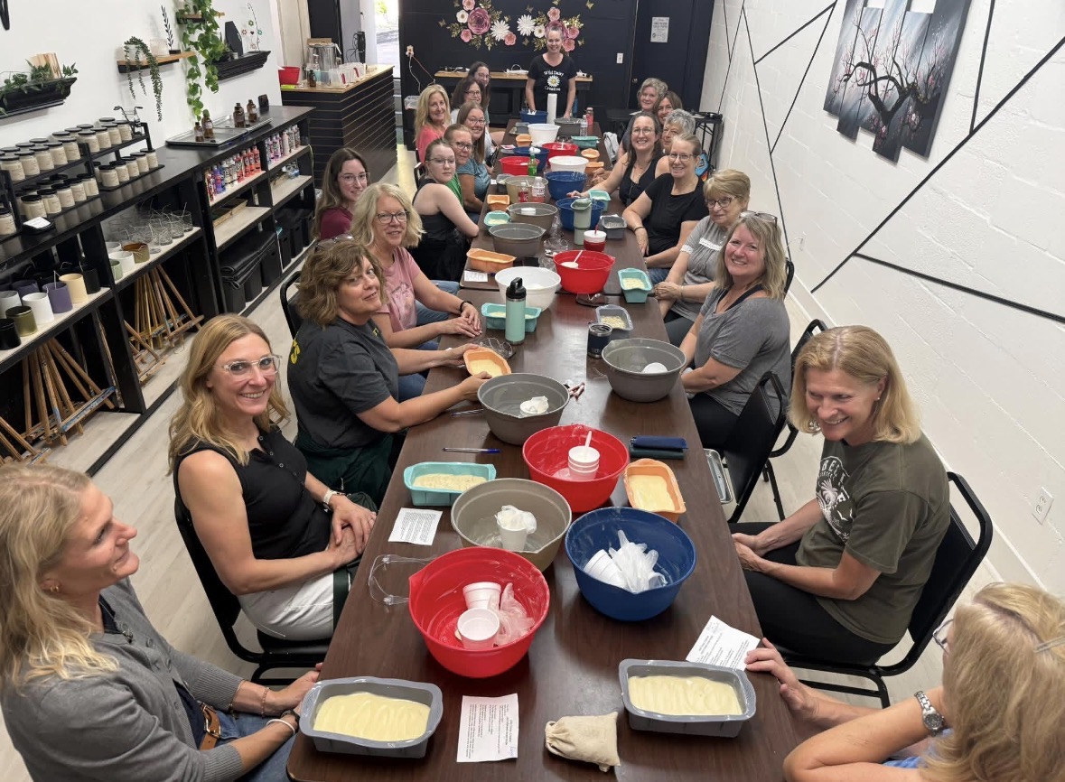 Group of women sitting around a long table with baking supplies in a room with shelves and wall art.