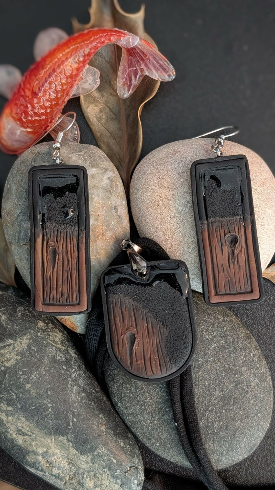 Three wooden and metal keychains on rocks, with a red and pink flower in the background.