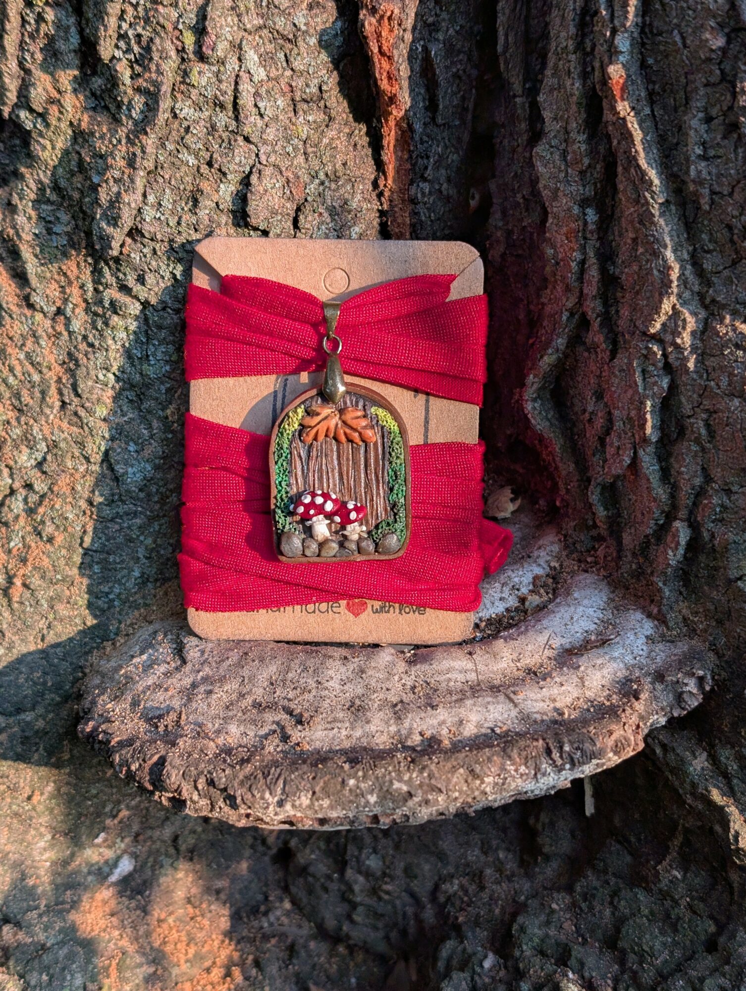 Decorative keychain with a small birdcage and flowers hangs from a red fabric wrapped around a tree trunk, on a wooden surface.