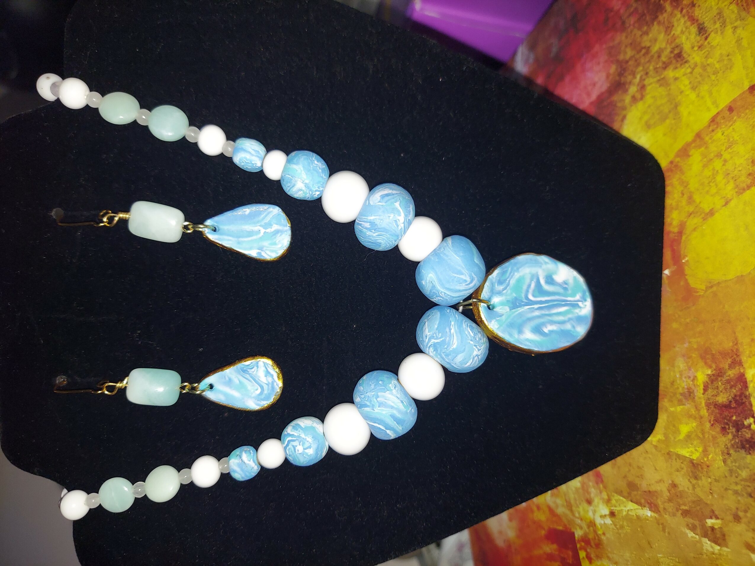 Necklace with white and blue beads, including a large blue pendant, on a black display stand.