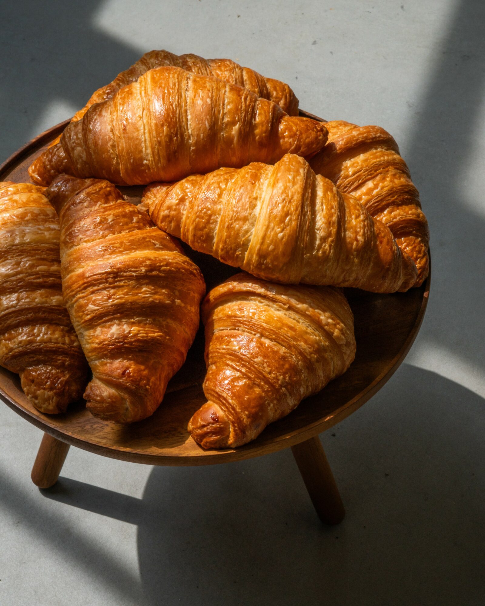 Seven croissants in a bowl on a table with shadows, viewed from above.