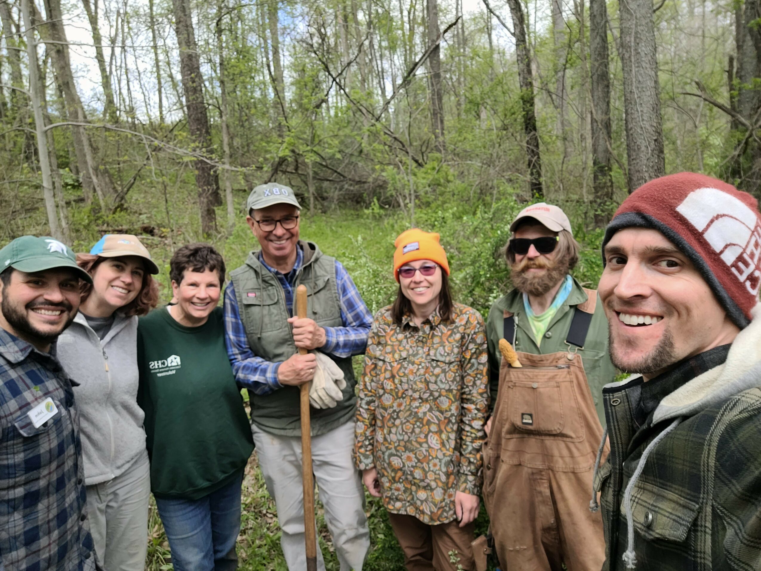 Group of seven people outdoors in a forest, smiling and posing for a photo.