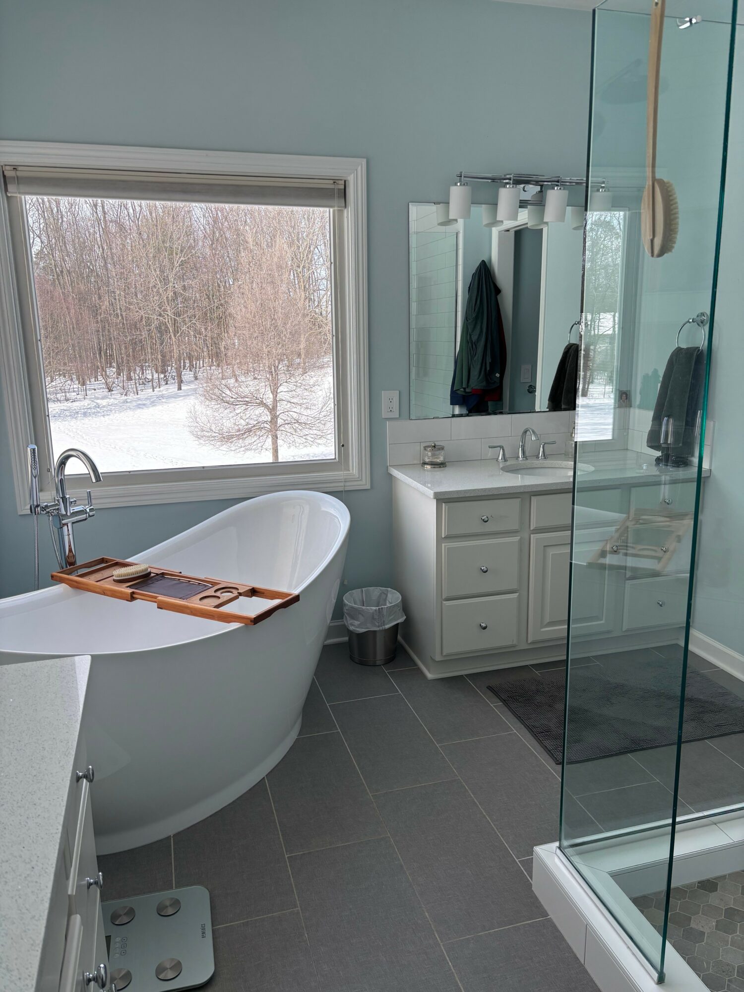 Bathroom with bathtub, window showing outdoor trees, glass shower enclosure, and vanity with mirror.