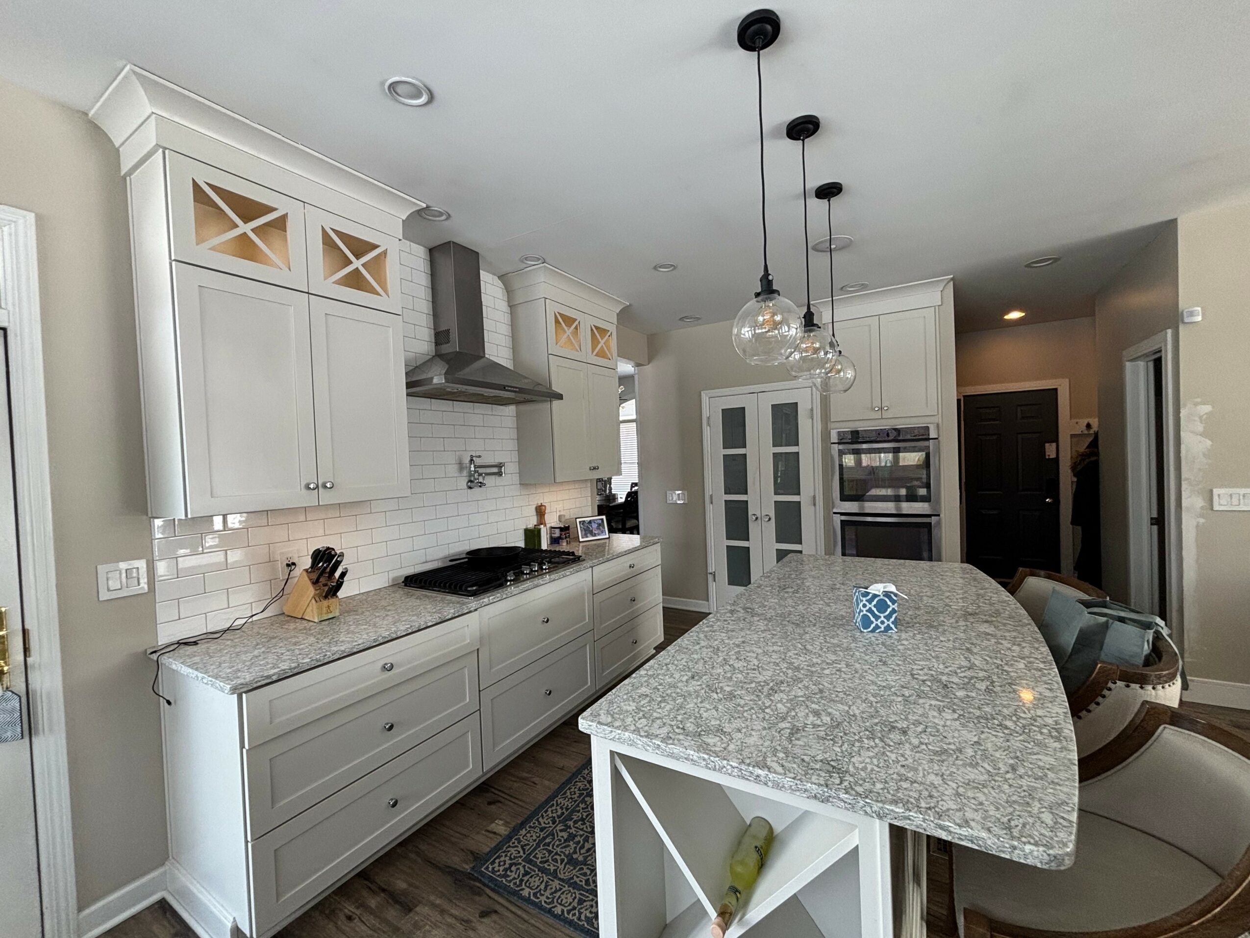 Kitchen with white cabinets, granite island, pendant lights, and appliances, viewed from the right side.