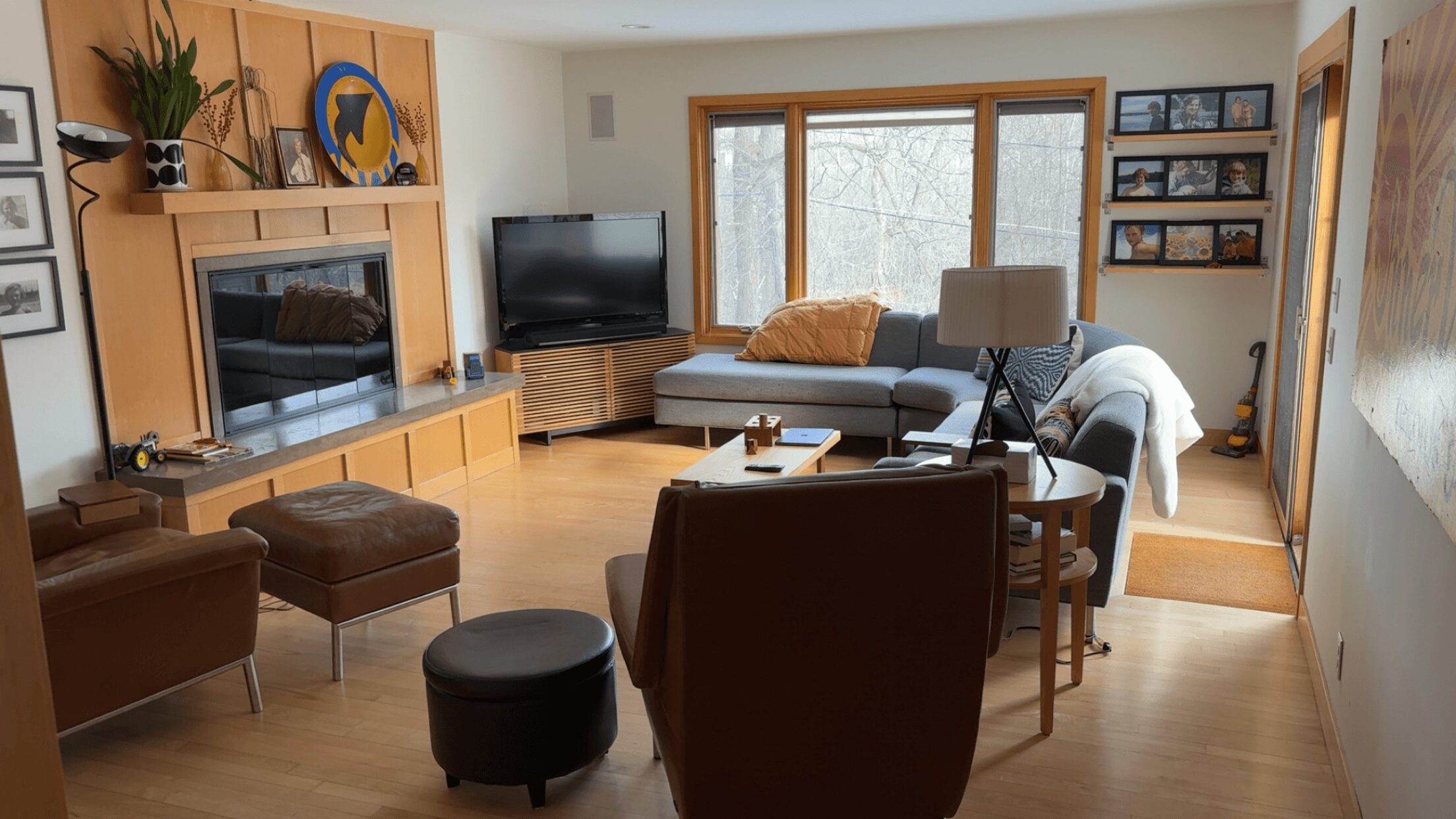 Living room with large window, sofa, armchair, TV, and wooden furniture, decorated with plants and artwork.
