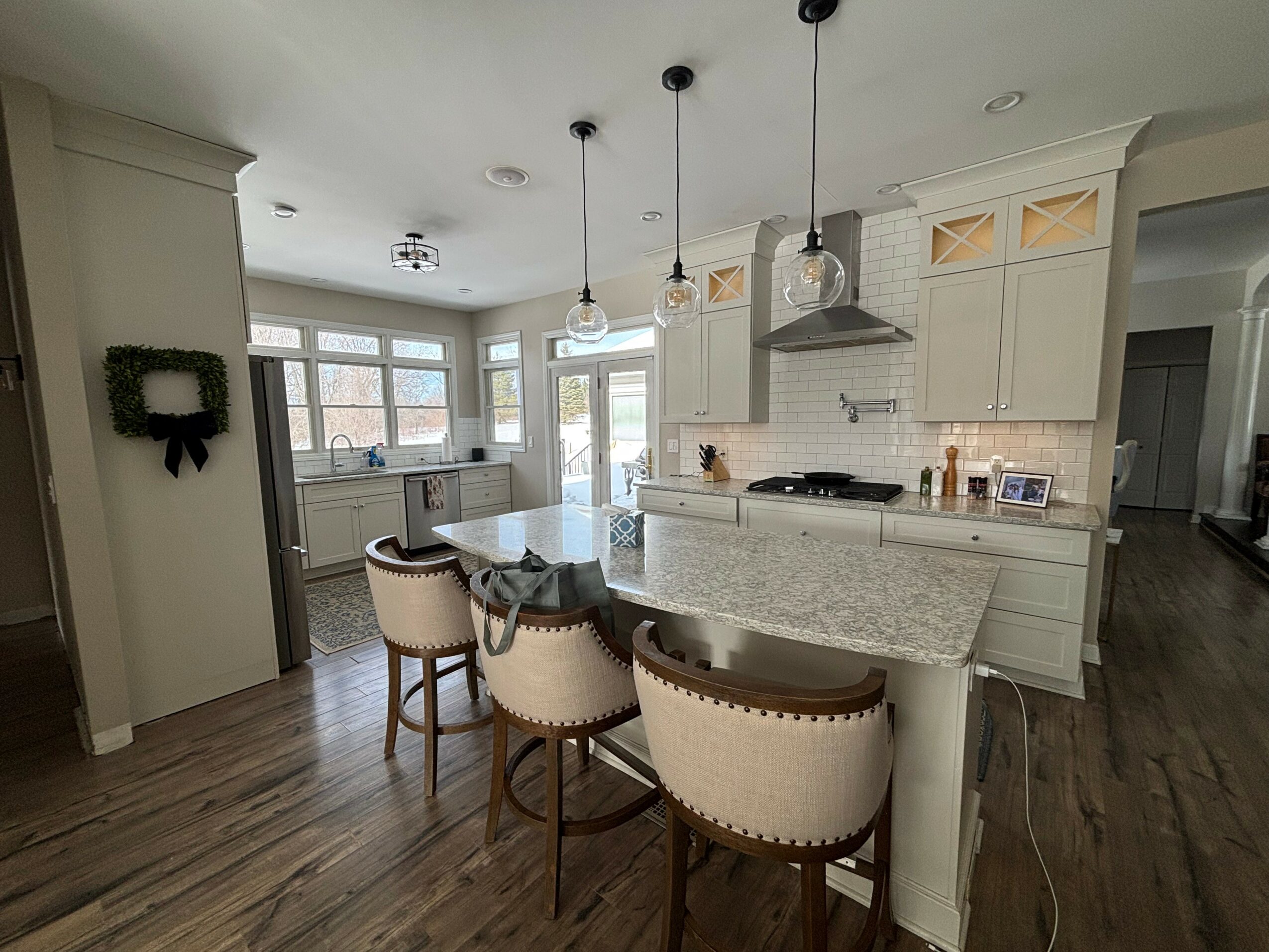 Kitchen with white cabinets, island with seating, pendant lights, and a view of the dining area and windows.