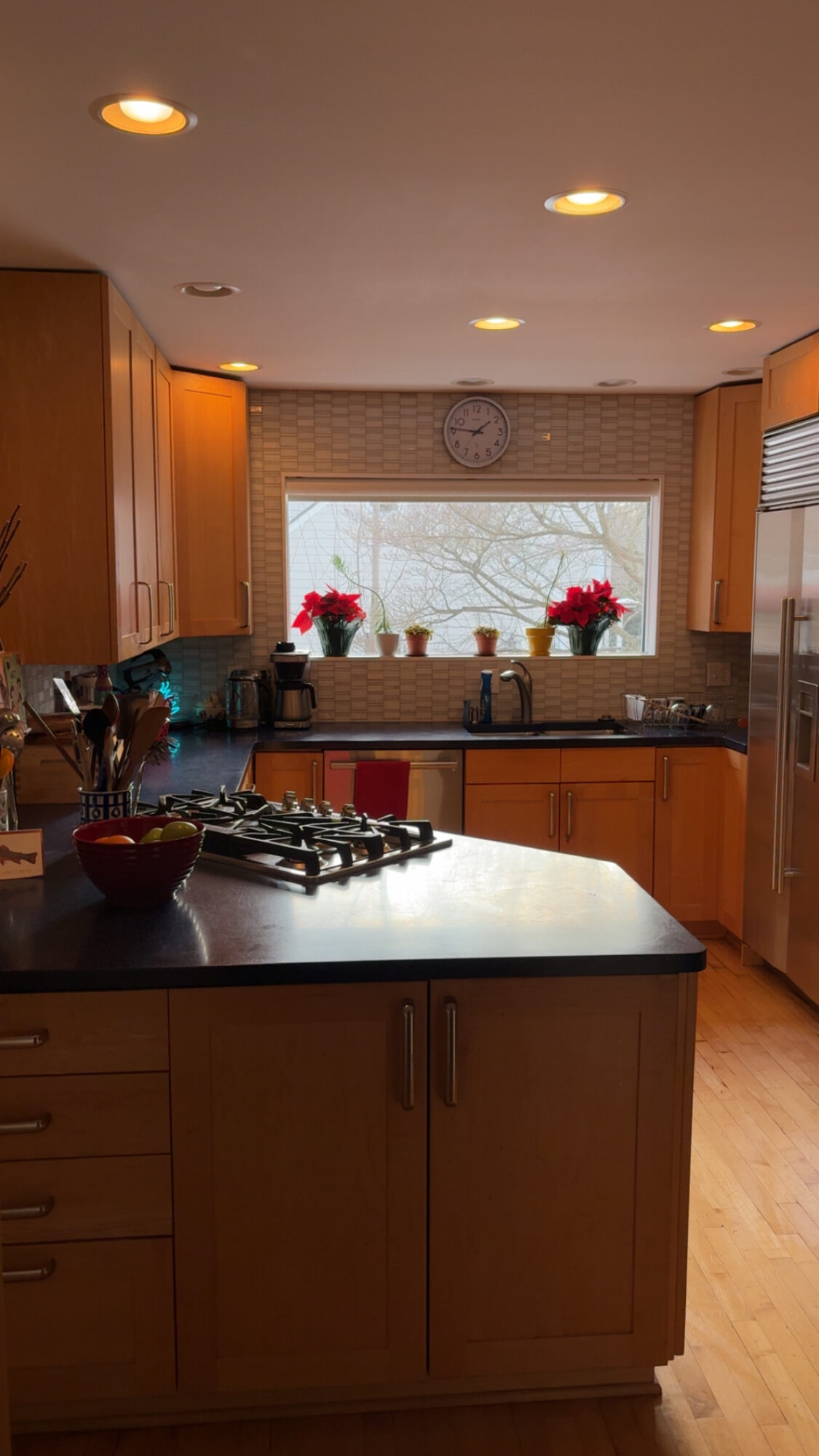 Kitchen with wooden cabinets, a window with flowers, and a countertop with a bowl and stove.