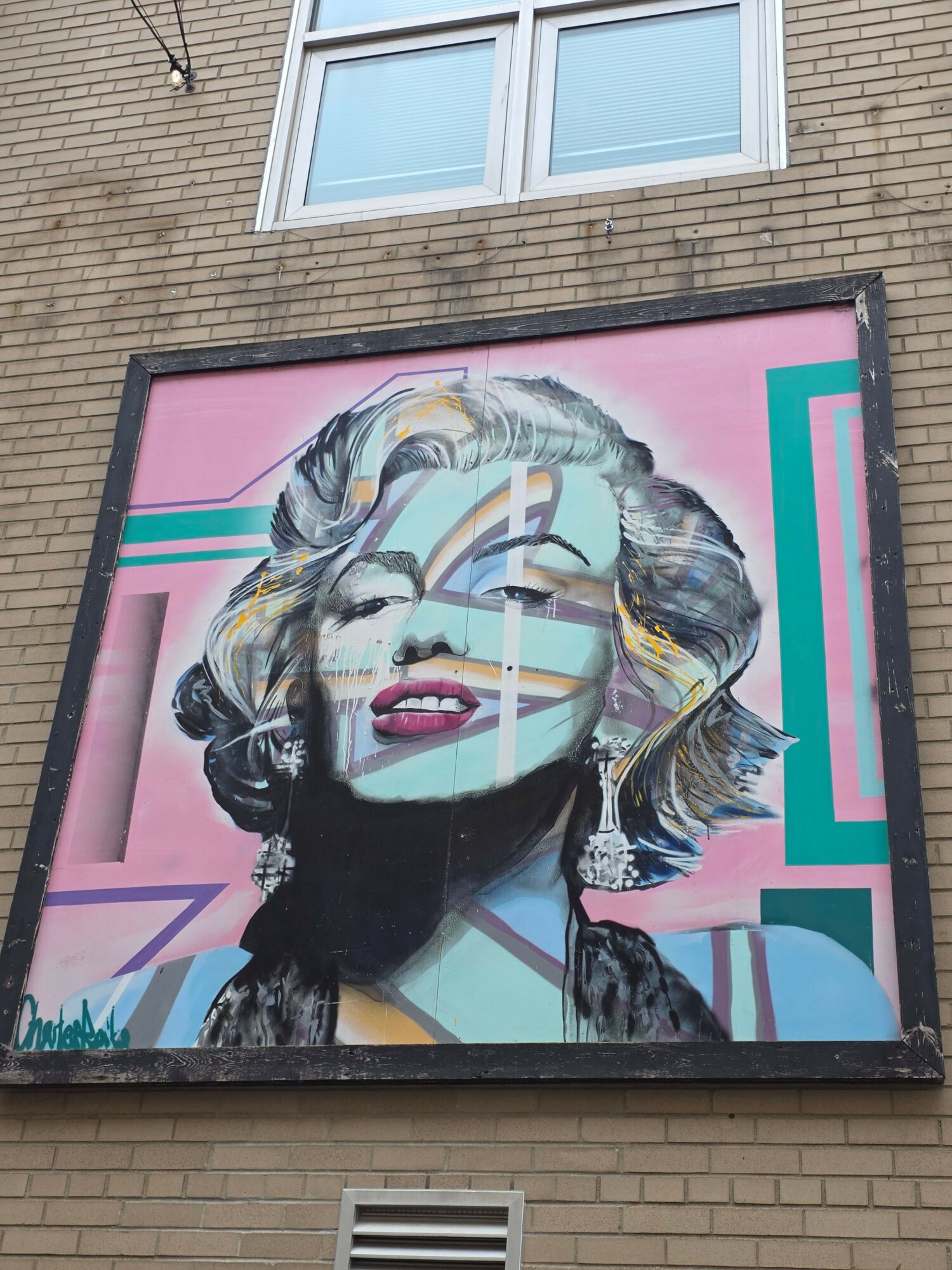 Colorful portrait of a woman with styled hair and makeup, painted on a large outdoor wall, with geometric background elements.