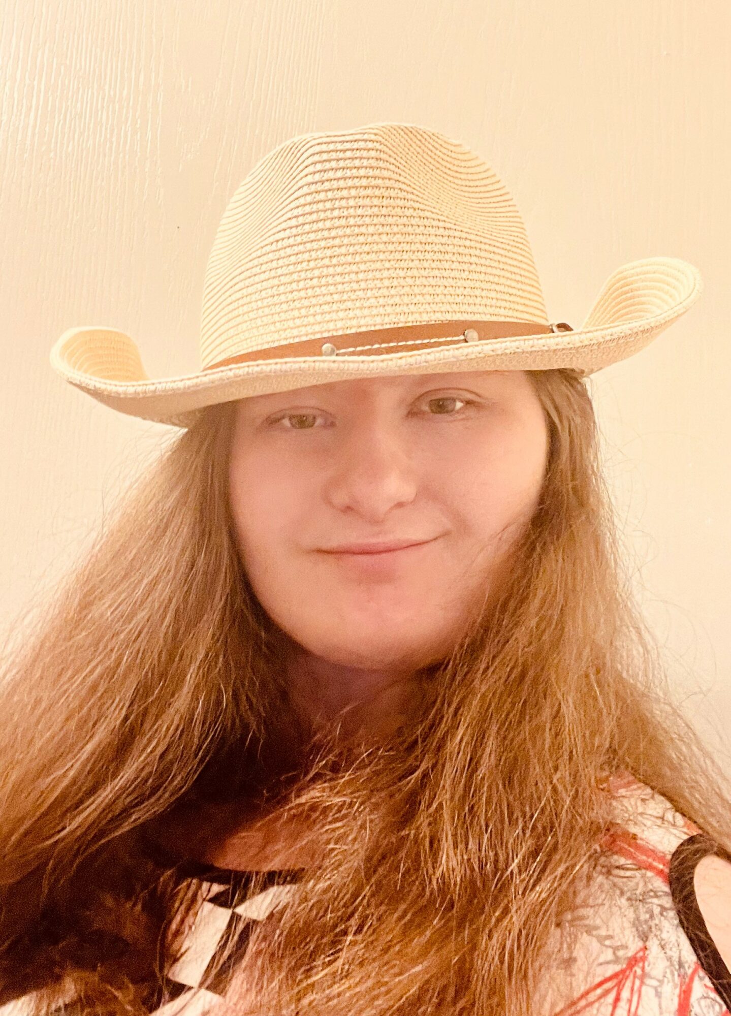 Person with long hair wearing a wide-brimmed hat, smiling slightly, against a plain background.