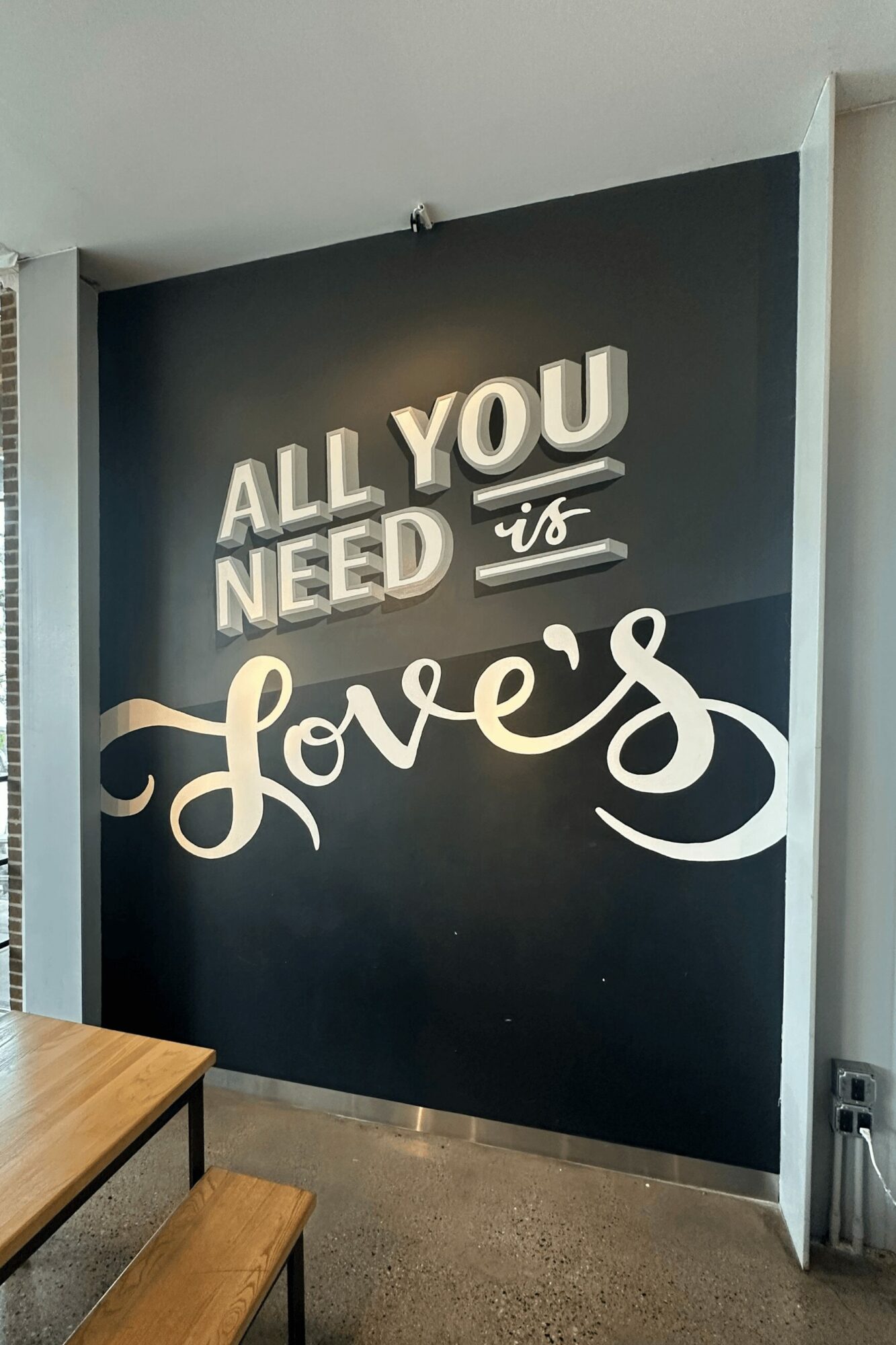 Wall with illuminated text reading 'All you need is love' in a cafe or similar setting.