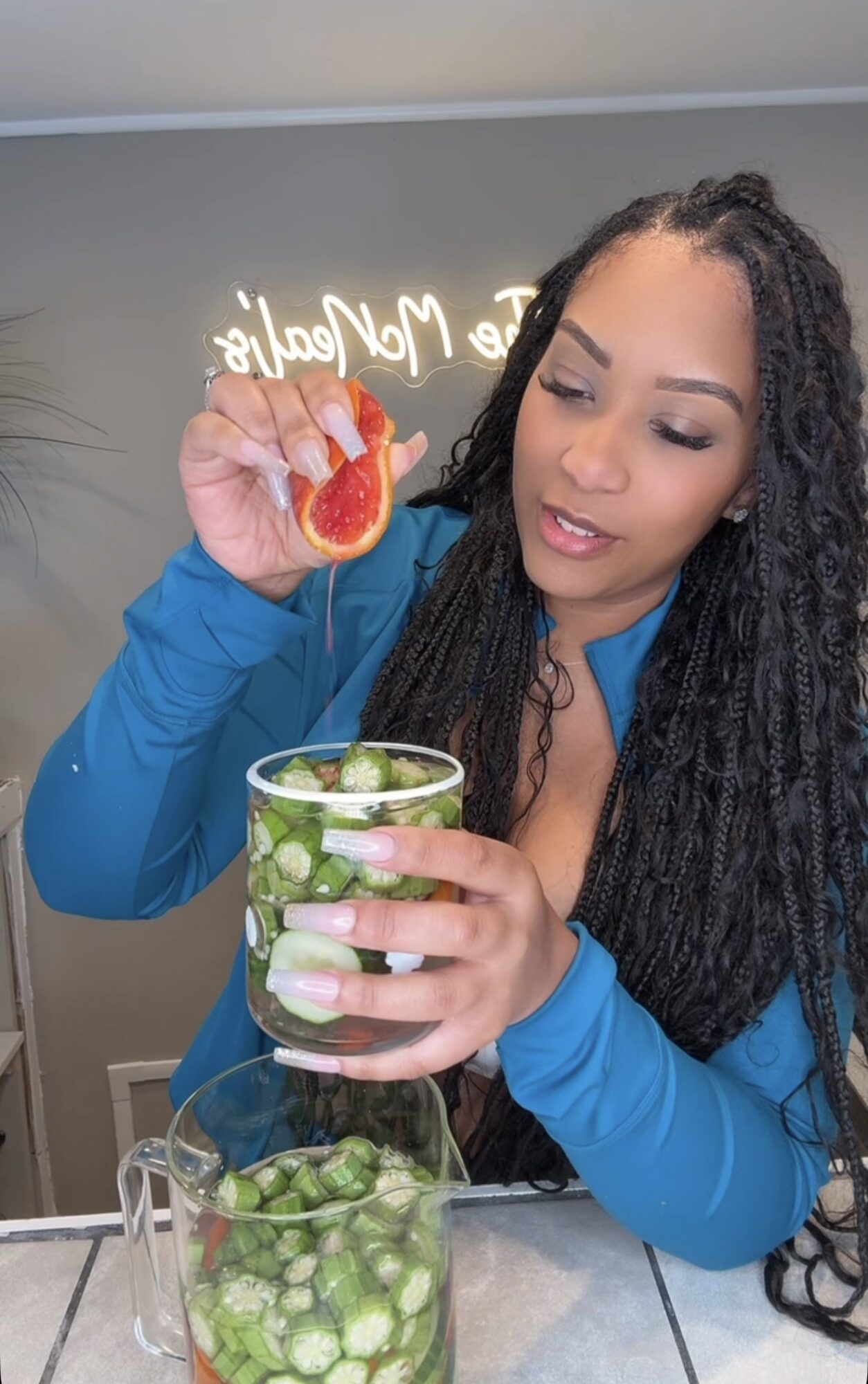 Woman with long curly hair holds a strawberry over a glass of cucumber slices, with a bowl of cucumber slices nearby.