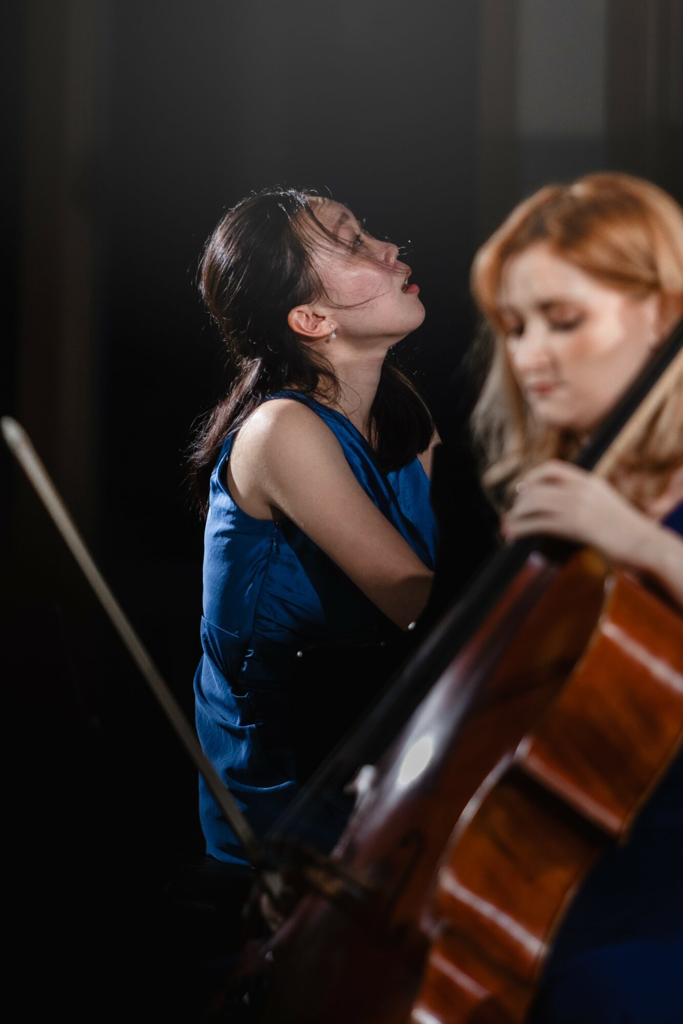 Two women playing string instruments, one with dark hair and the other with red hair, in a dimly lit setting.