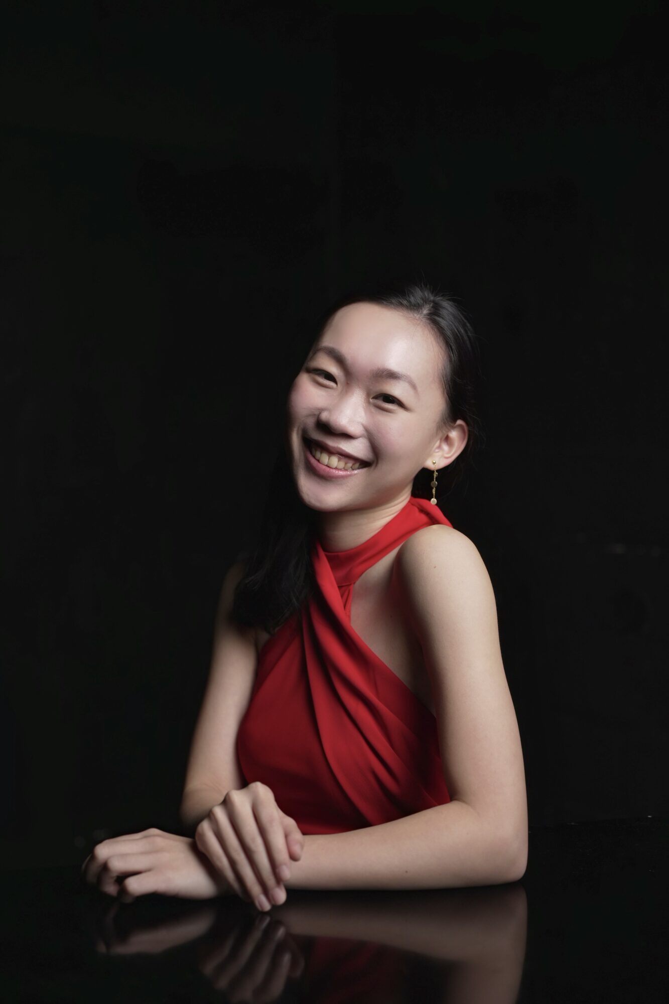 Young woman with long dark hair smiling, wearing a red sleeveless top, against a dark background.