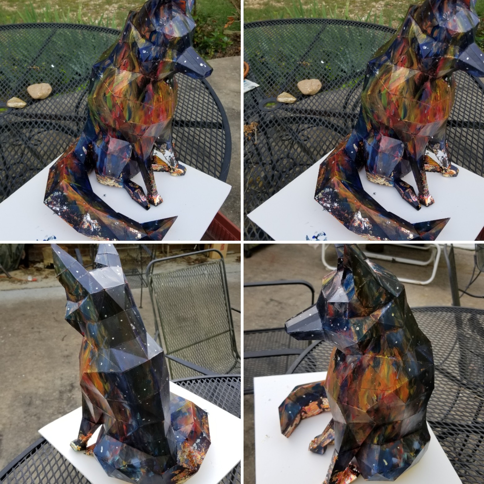 Colorful abstract sculpture of a dog on a white surface outdoors, with a metal table and chairs in the background.