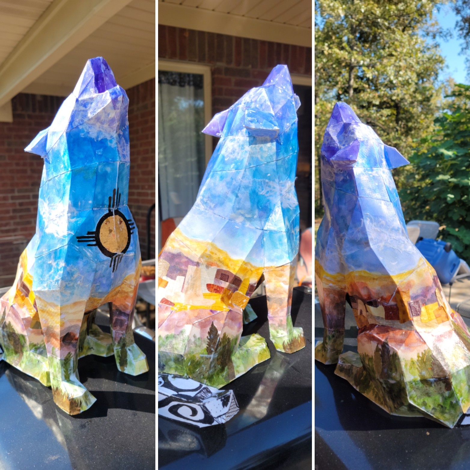 Colorful painted rock sculpture of a dog, outdoors, with trees and sky in background.